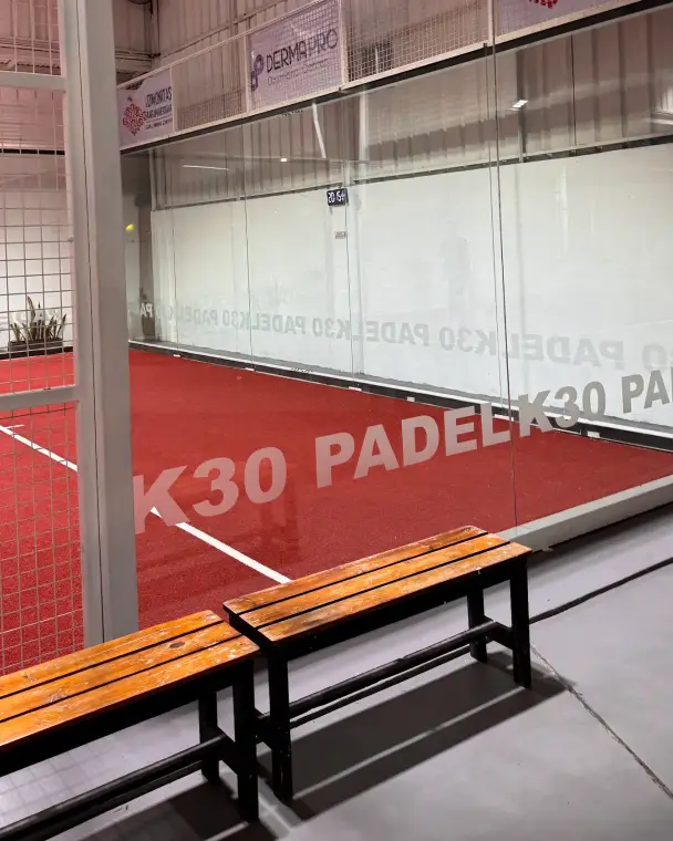 Wooden benches beside the court with K30 Padel lettering on the glass